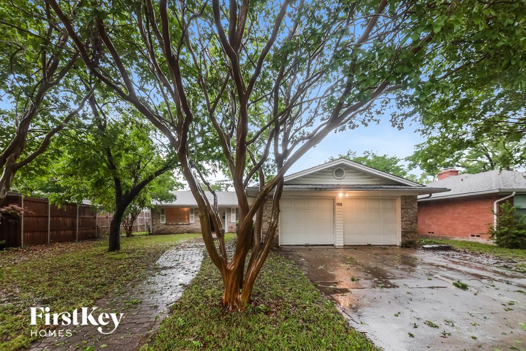 A tree in front of a house with a garage door.