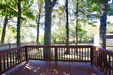 A wooden deck with a railing and trees in the background.