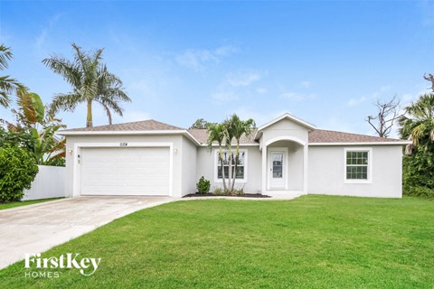 a white house with a lawn and palm trees
