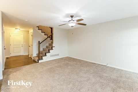 A spacious room with a carpeted floor, a ceiling fan, and a staircase with a wooden banister.