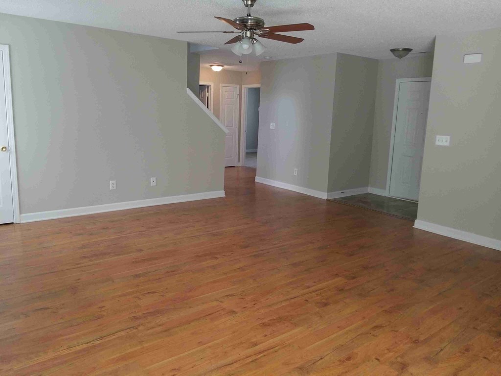an empty living room with wooden floors and a ceiling fan
