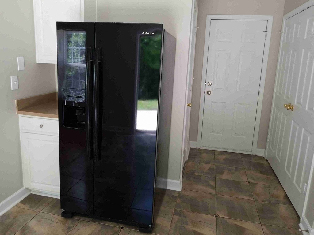 a black refrigerator in a kitchen with white cabinets