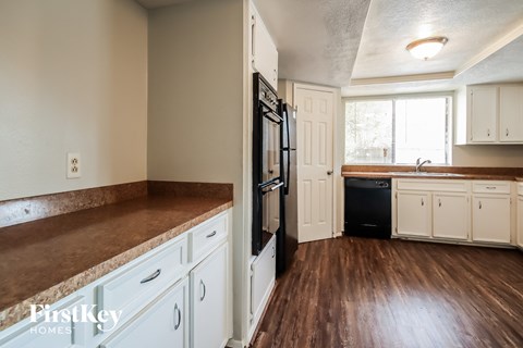 a kitchen with white cabinets and black appliances and a wood floor