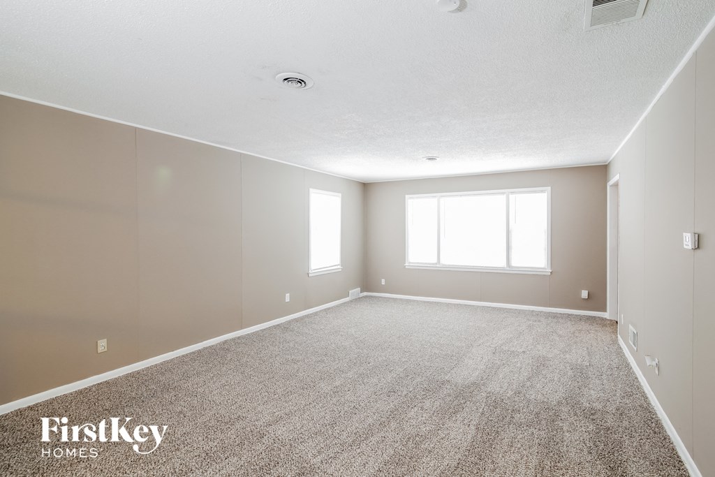 A spacious room with a carpeted floor and two windows.