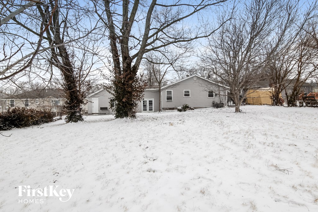 A snow-covered field with a house and trees in the background.