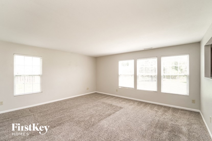 A spacious room with a carpeted floor and three windows.