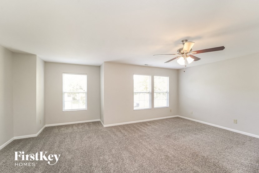 A spacious room with a ceiling fan and two windows.