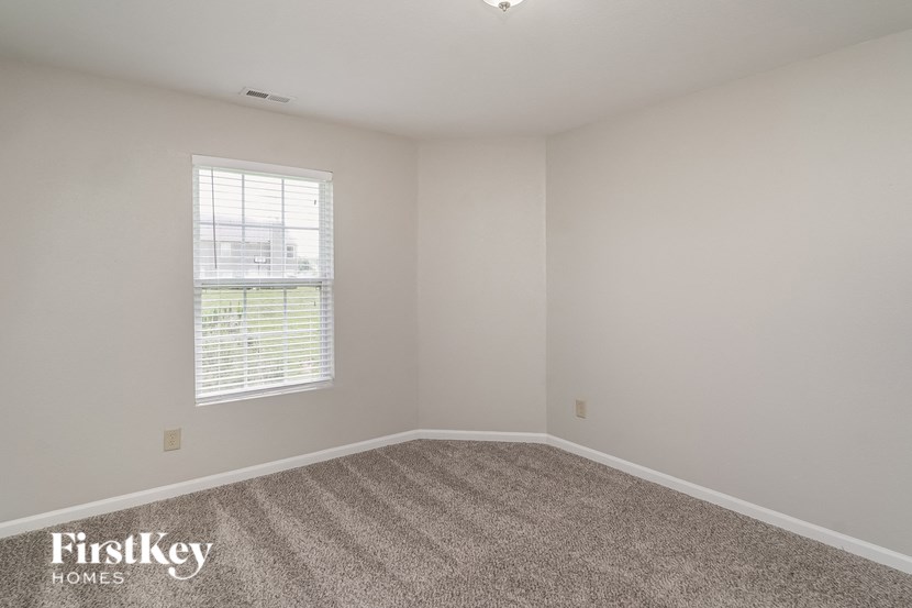A room with a carpeted floor and a window with blinds.