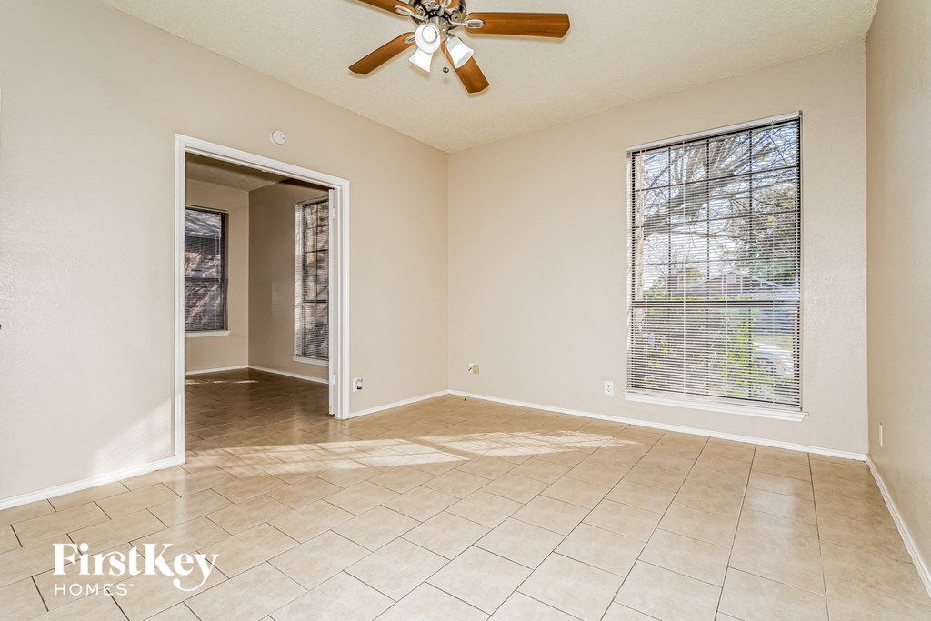A spacious room with a ceiling fan and a sliding glass door leading to a balcony.