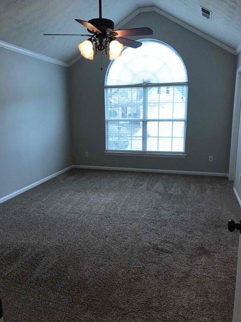 A room with a ceiling fan and a window with a view of a building outside.