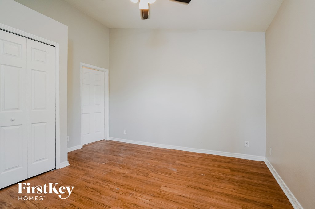 A room with wooden floors and white walls, with a ceiling fan and two doors.