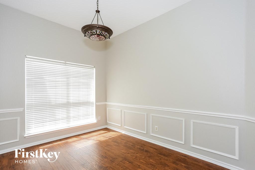 A room with a wooden floor, a window with blinds, and a chandelier hanging from the ceiling.