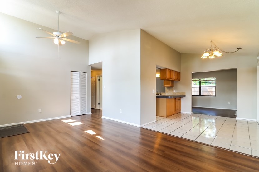 A spacious living room with wood flooring and a kitchen area in the background.