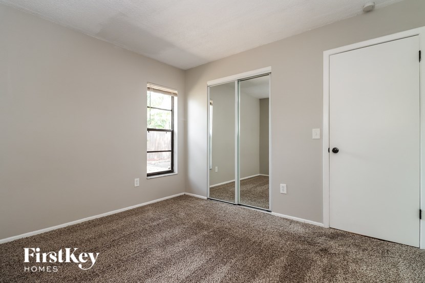 A room with a carpeted floor, a white door, a window, and a mirrored closet door.
