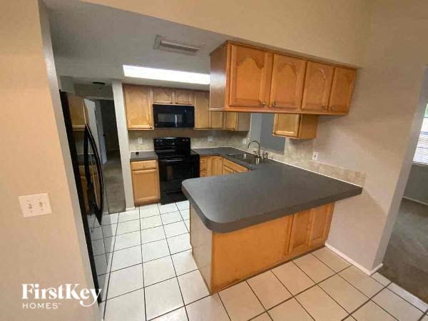 A kitchen with a black fridge, black stove, and wooden cabinets.