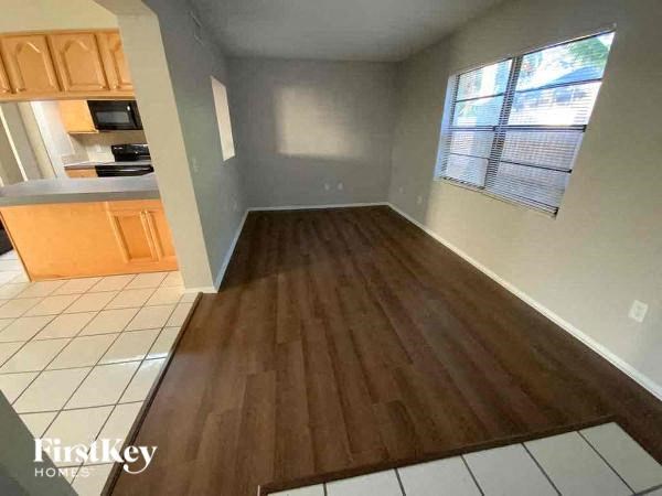 A room with wooden flooring and a kitchen area with white tiles.