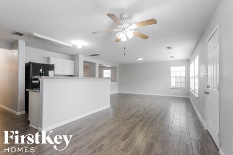 A spacious, empty room with a ceiling fan and wooden flooring.