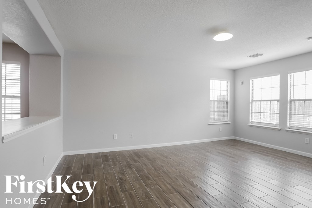 A spacious room with wooden flooring and windows on the wall.