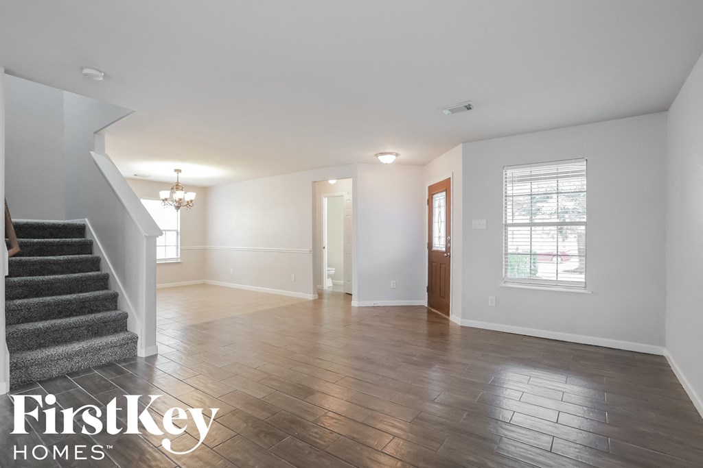A spacious room with wooden flooring and a staircase on the left side.