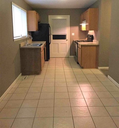 A kitchen with a black refrigerator and white tiled floor.