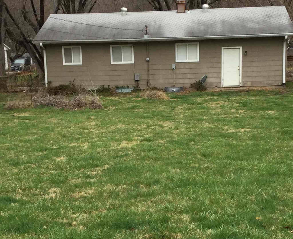 A small house with a white door and windows is surrounded by a grassy area.