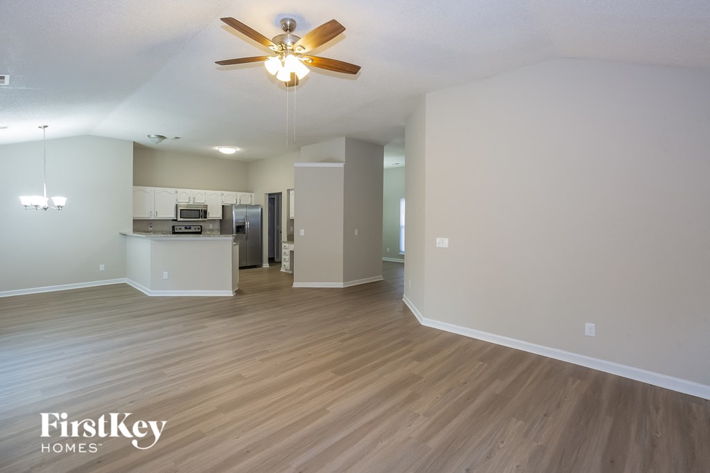an empty living room with a ceiling fan and a kitchen