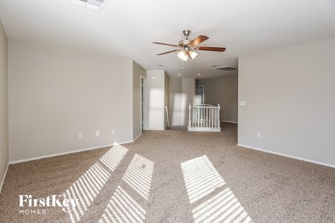 a spacious living room with carpet and a ceiling fan