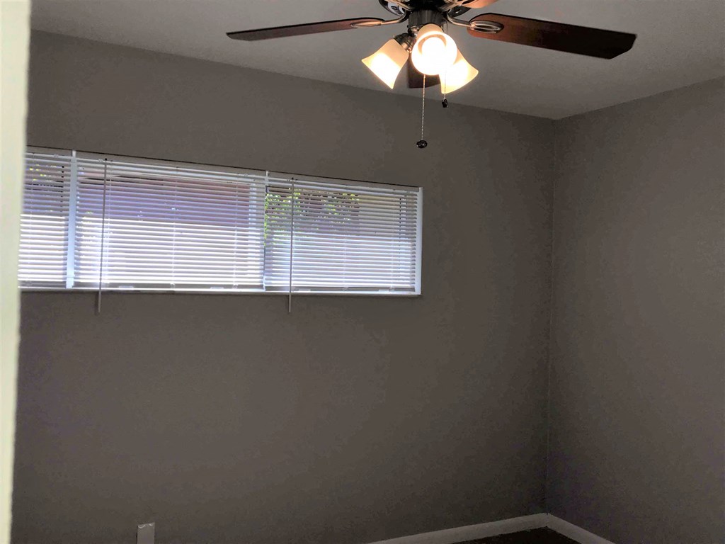 A room with a ceiling fan and a window with blinds.