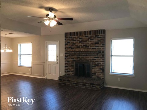 an empty living room with a brick fireplace and a ceiling fan