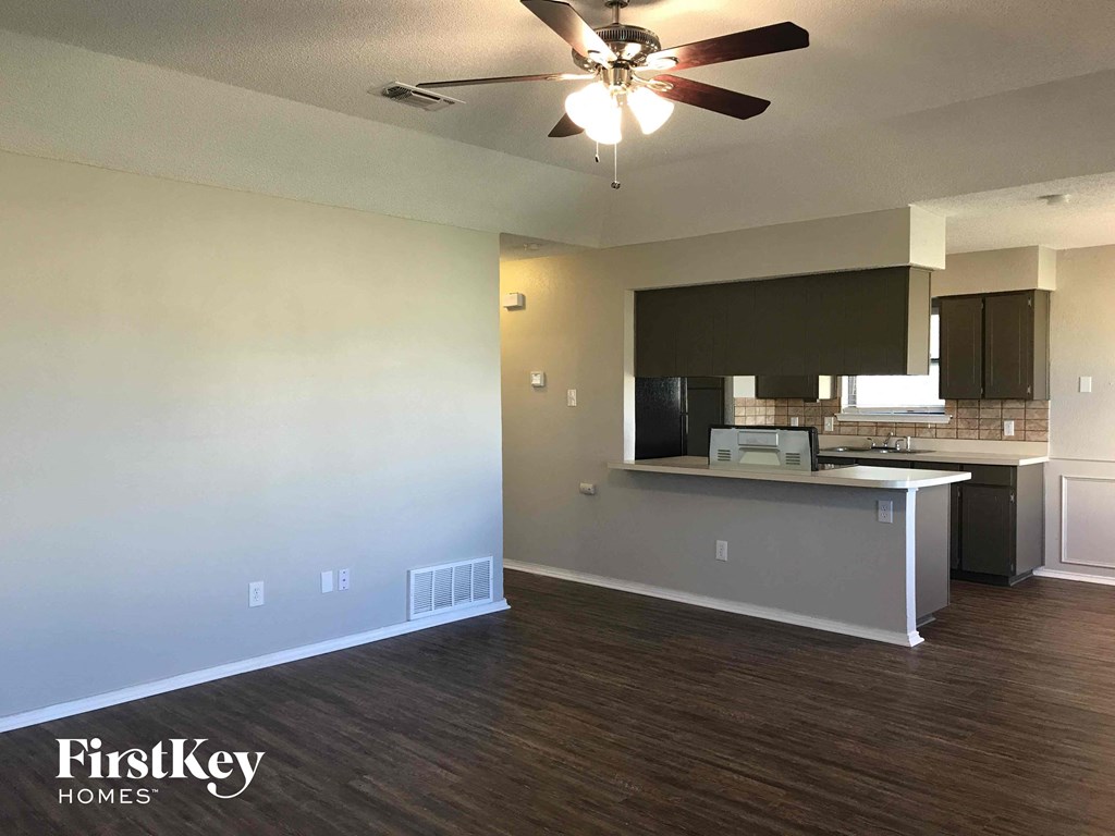 an empty living room and kitchen with a ceiling fan