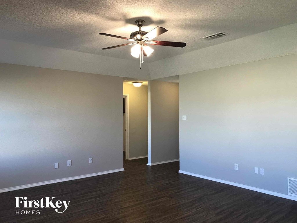 an empty living room with a ceiling fan and white walls