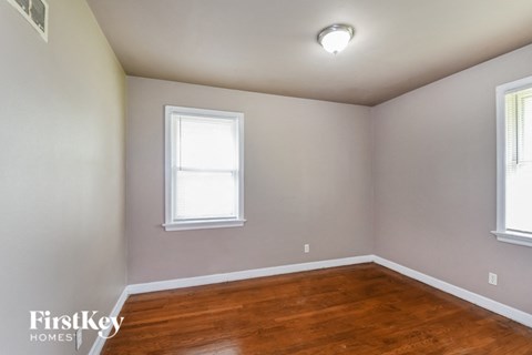 a bedroom with a wood floor and two windows