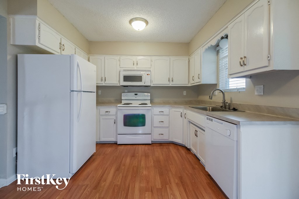 a kitchen with white cabinets and white appliances and a wooden floor
