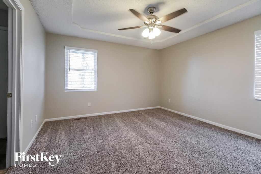 the living room of an empty home with carpet and a ceiling fan