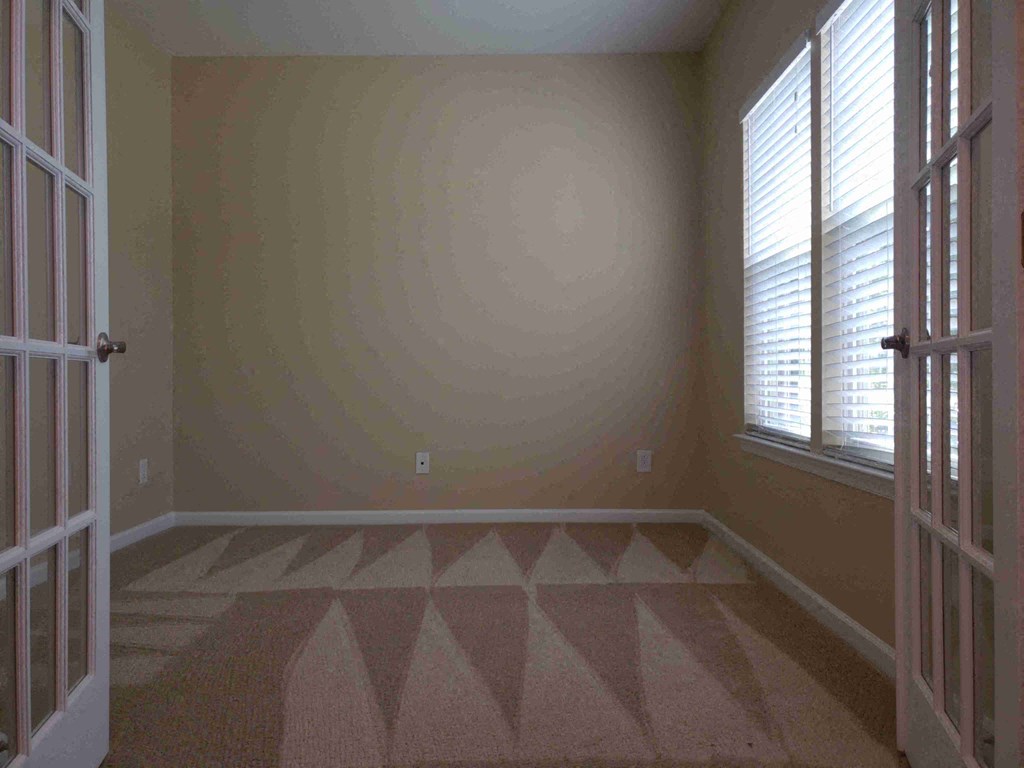 A room with a carpeted floor and a window with blinds.