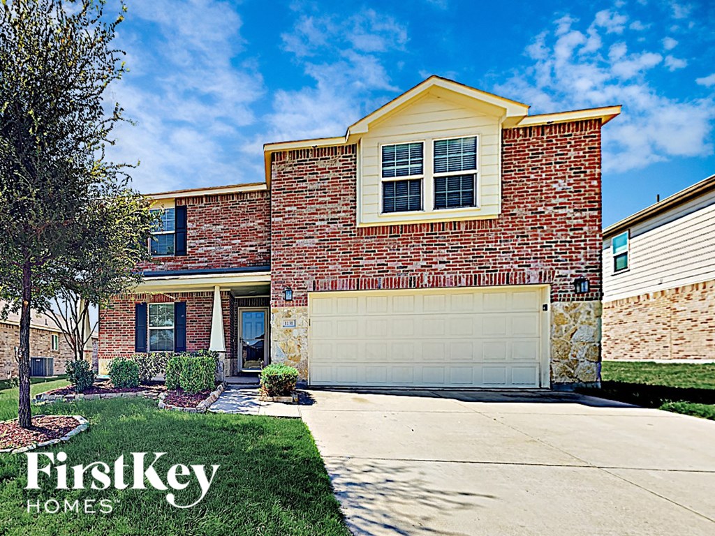 A brick house with a garage door and a tree in front.