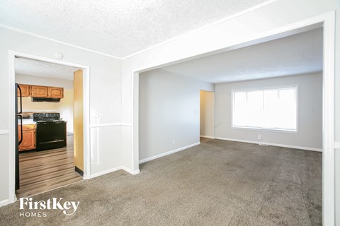 A spacious room with a carpeted floor and a window with white curtains.