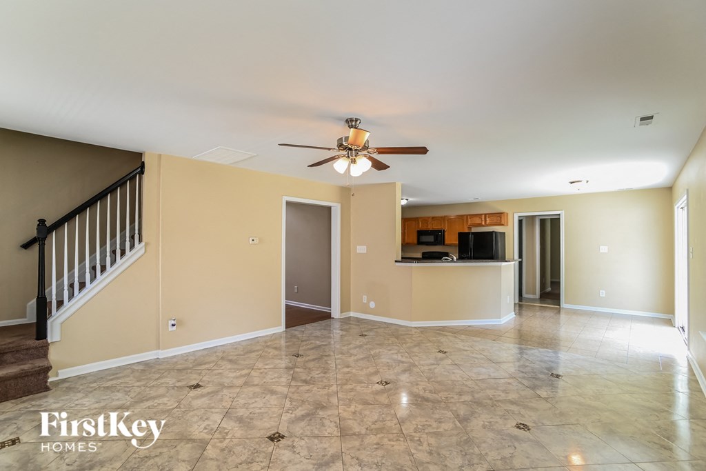 an empty living room with a ceiling fan and a kitchen