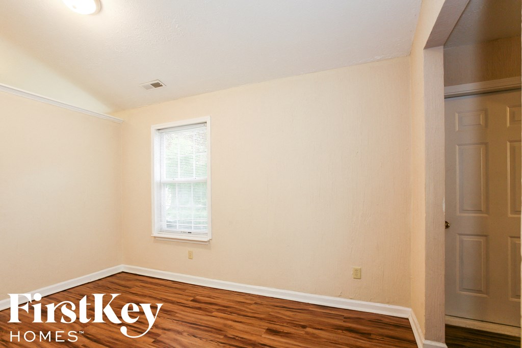 a bedroom with a hardwood floor and white walls and a window