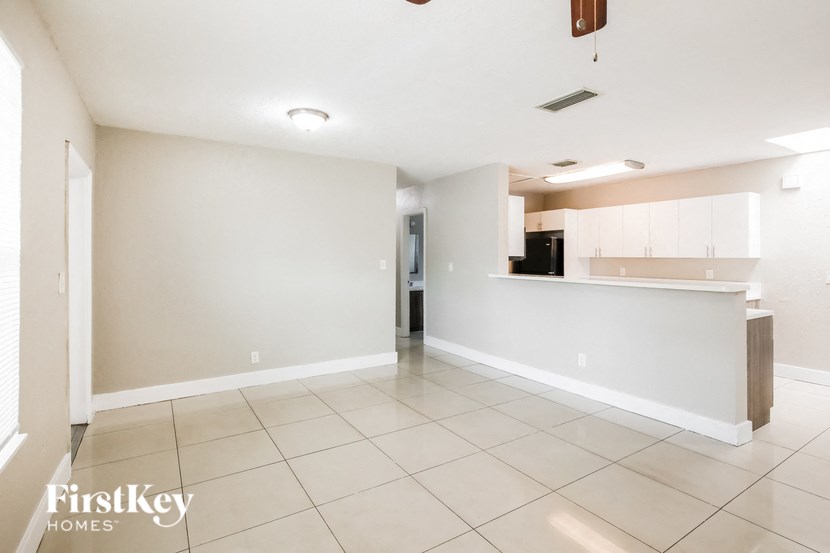 an empty living room and kitchen with white tile floors and white cabinets
