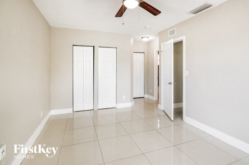 an empty living room with a ceiling fan and doors to three closets