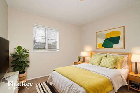 A bedroom with a bed, a potted plant, and a painting on the wall.