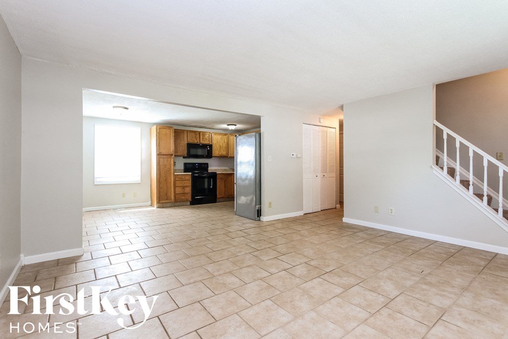 an empty living room with a staircase and a kitchen