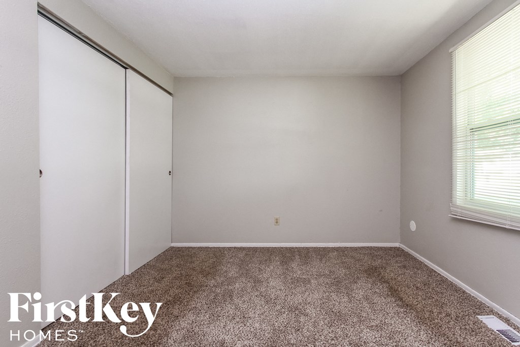 a bedroom with white walls and carpet and a window
