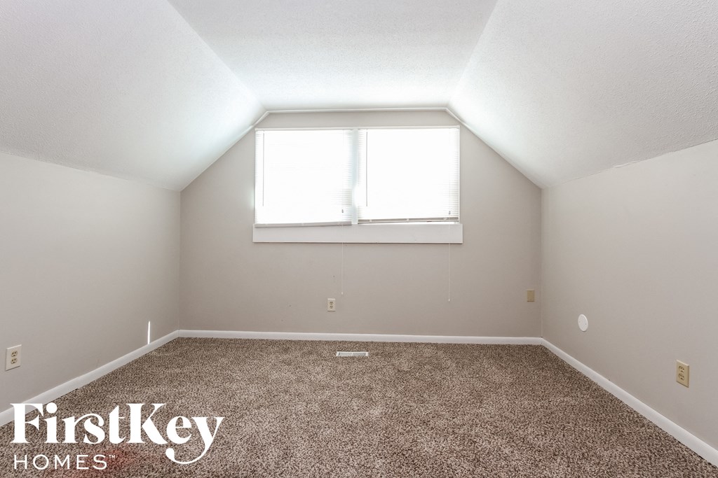 the bedroom of a small house with carpet and a window