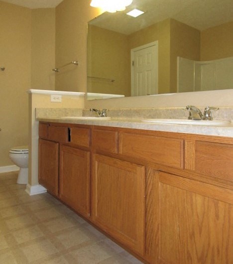 A bathroom with a toilet, sink, and wooden cabinets.