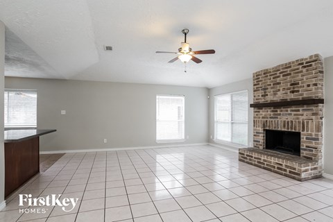 A spacious living room with a brick fireplace and a ceiling fan.