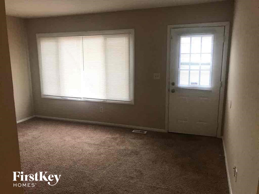 A room with a carpeted floor, a door, and a window with blinds.