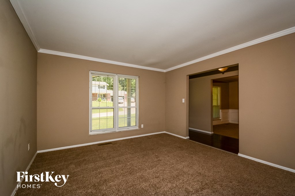 A room with a carpeted floor and a window with a view of a street.