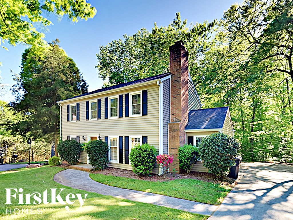 a yellow house with a brick chimney and a sidewalk in front of trees